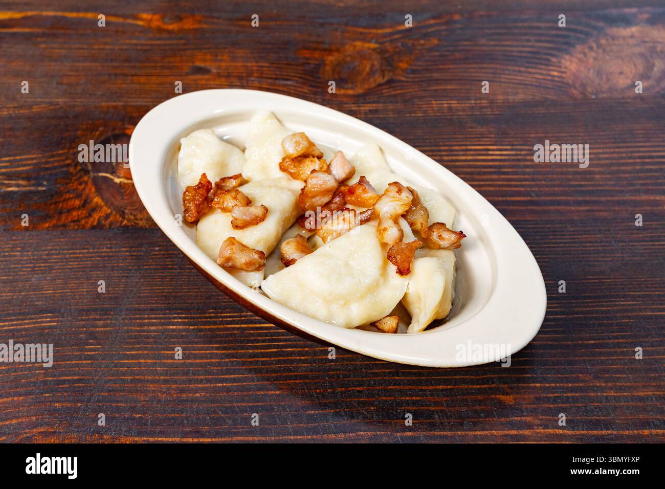 Deliziosi gnocchi ripieni di patate e formaggio ricoperti di pancetta croccante sono presentati in un piatto bianco su un rustico tavolo di legno, invitante a un richiamo Foto Stock