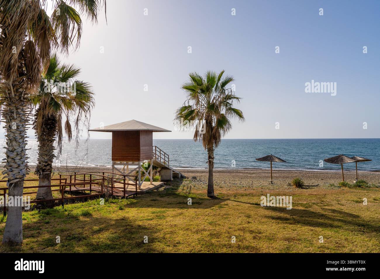 Vista panoramica della torre del bagnino in legno che si affaccia sul tranquillo Mar Mediterraneo, splendidamente incorniciata da palme sulla tranquilla spiaggia nel sud di Cipro. Viaggio, Foto Stock