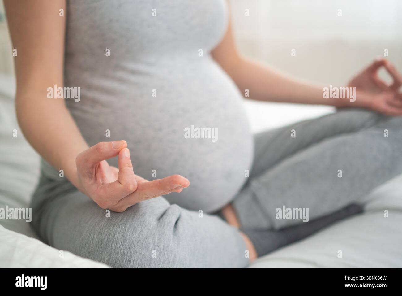 Donna incinta radiosa seduta sul letto, toccando amorevolmente la sua pancia in un ambiente domestico accogliente. Bella anticipazione della maternità e della nuova vita. Foto Stock