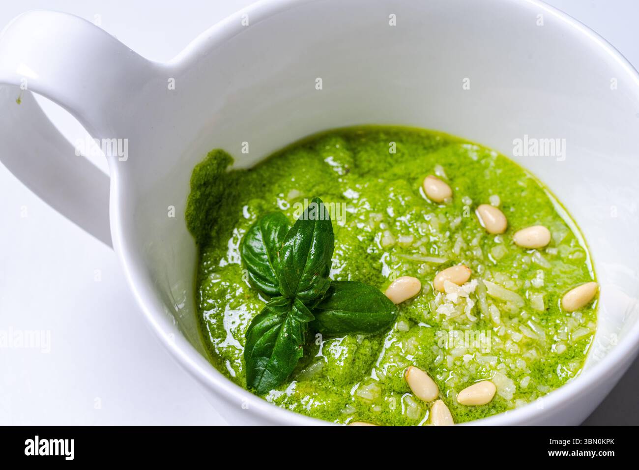 Salsa al pesto secondo una tradizionale ricetta italiana in una casseruola su sfondo bianco, decorata con basilico e pinoli. Foto di alta qualità Foto Stock