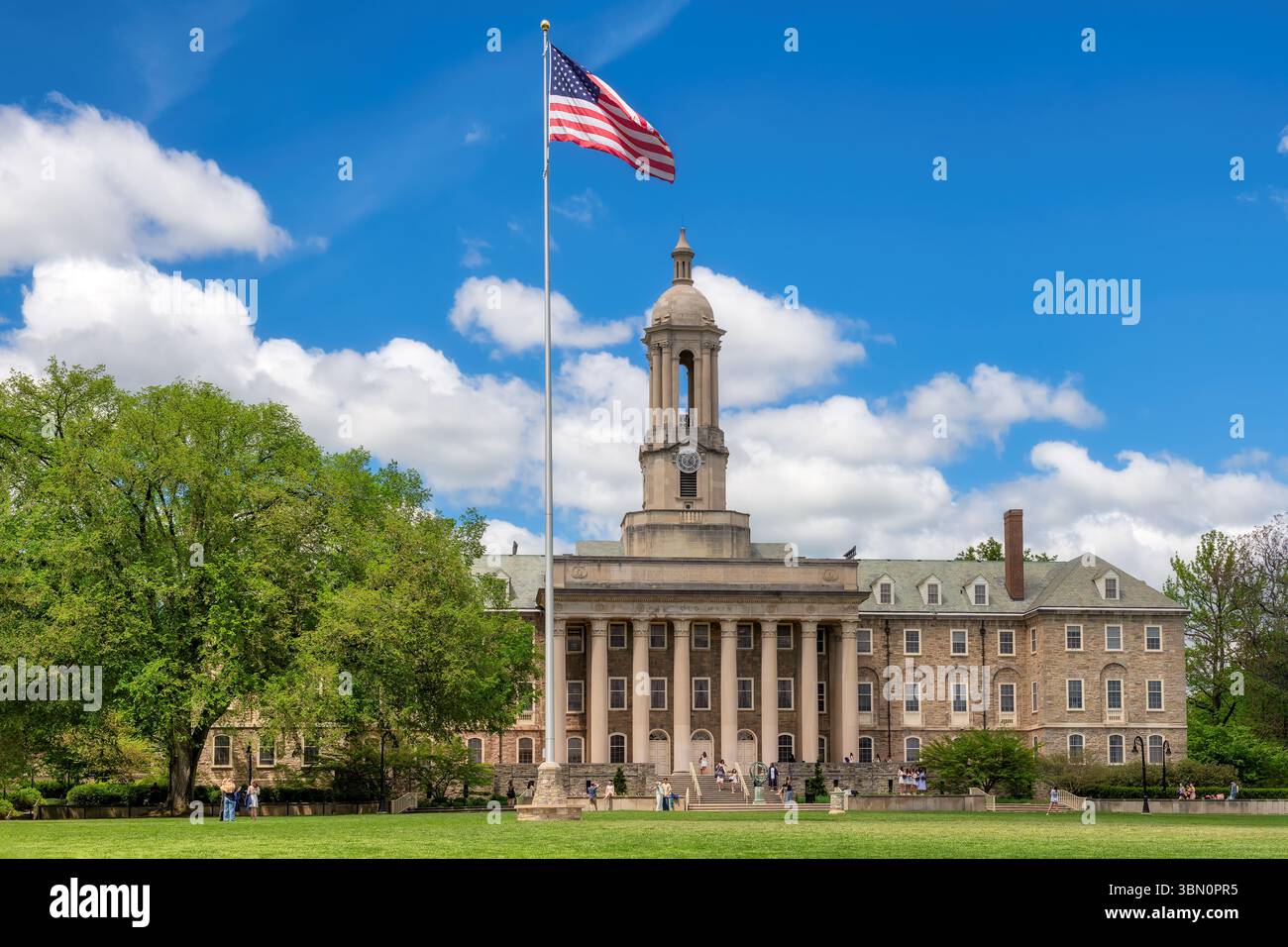 Il vecchio edificio principale nel campus della Penn State University e la bandiera americana nella giornata di sole primaverile, State College, Pennsylvania. Foto Stock
