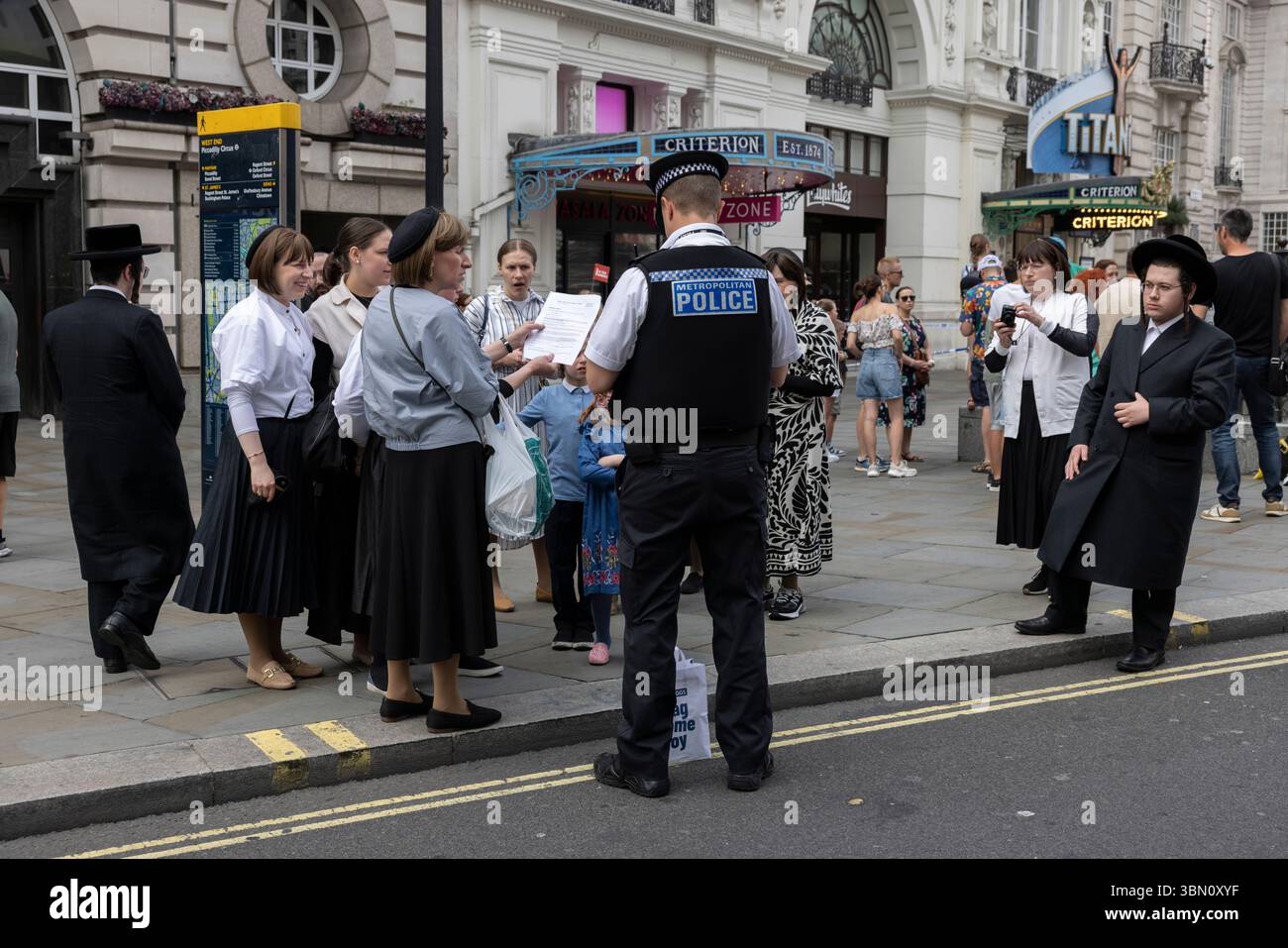 I turisti ebrei ricevono assistenza da un poliziotto metropolitano nel West End di Londra, Inghilterra, Regno Unito Foto Stock