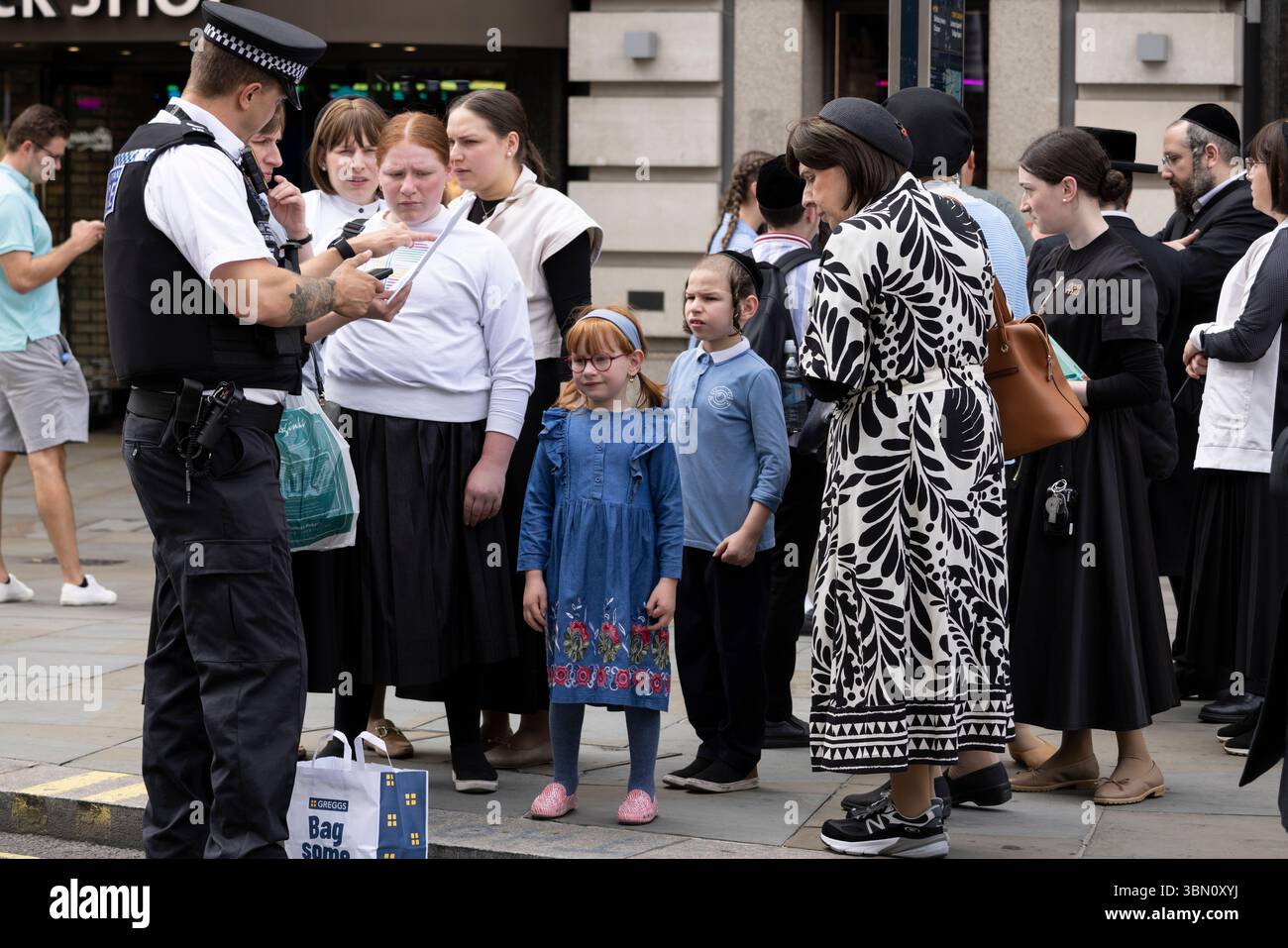 I turisti ebrei ricevono assistenza da un poliziotto metropolitano nel West End di Londra, Inghilterra, Regno Unito Foto Stock
