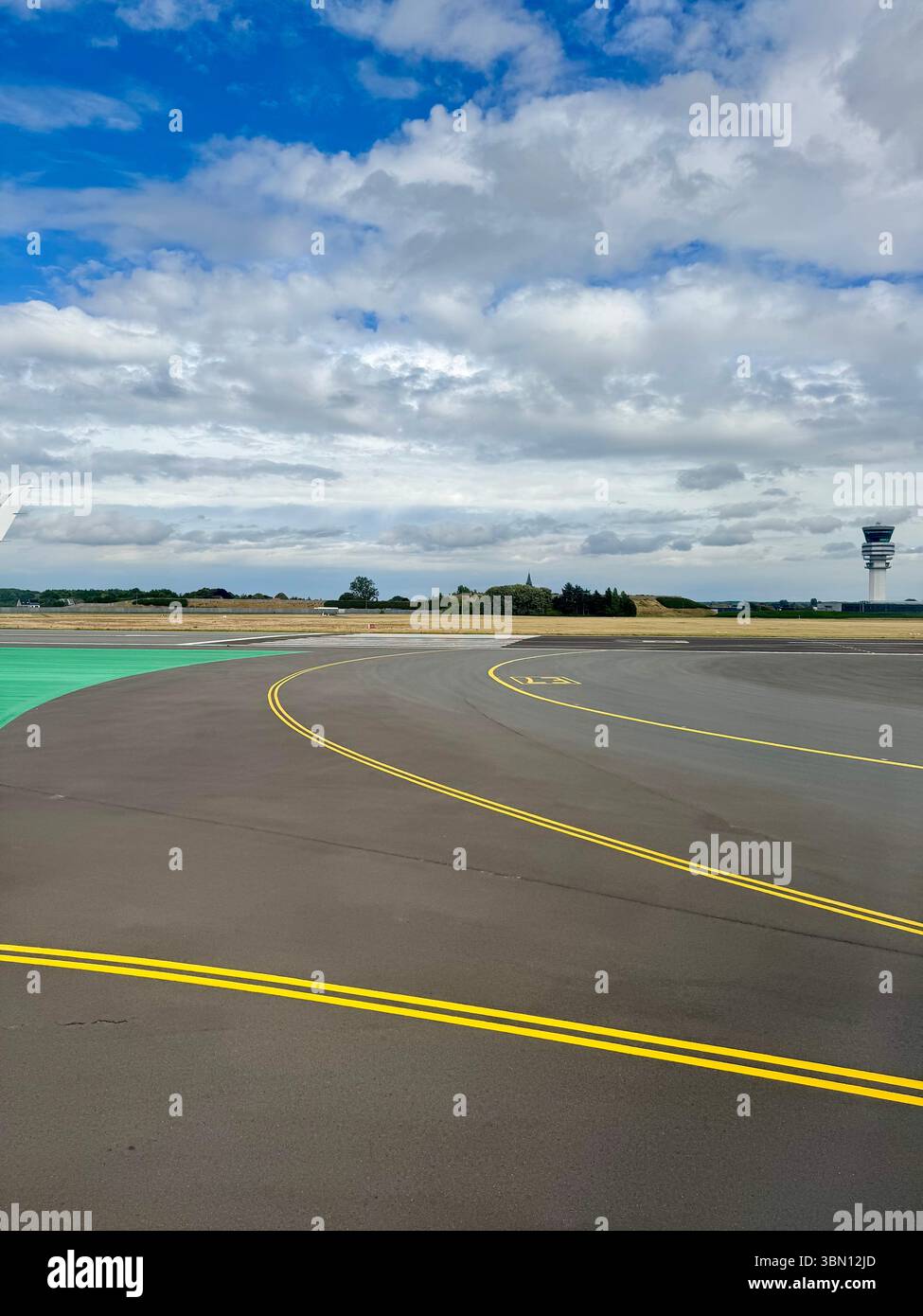 Via di rullaggio curva all'aeroporto di Bruxelles sotto un cielo nuvoloso con torre di controllo in lontananza. Vista grandangolare di una strada di rullaggio curva all'aeroporto di Bruxelles. - Immagine stock catturata con smartphone