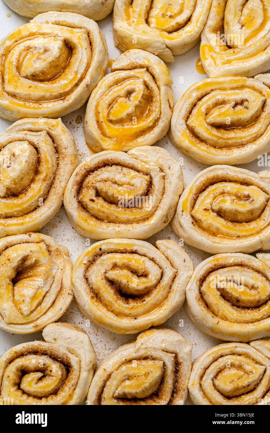 Preparare focaccine di pasta sfoglia alla cannella fatte in casa. Rotoli di impasto crudi ingrassati con tuorlo d'uovo. Foto di alta qualità Foto Stock