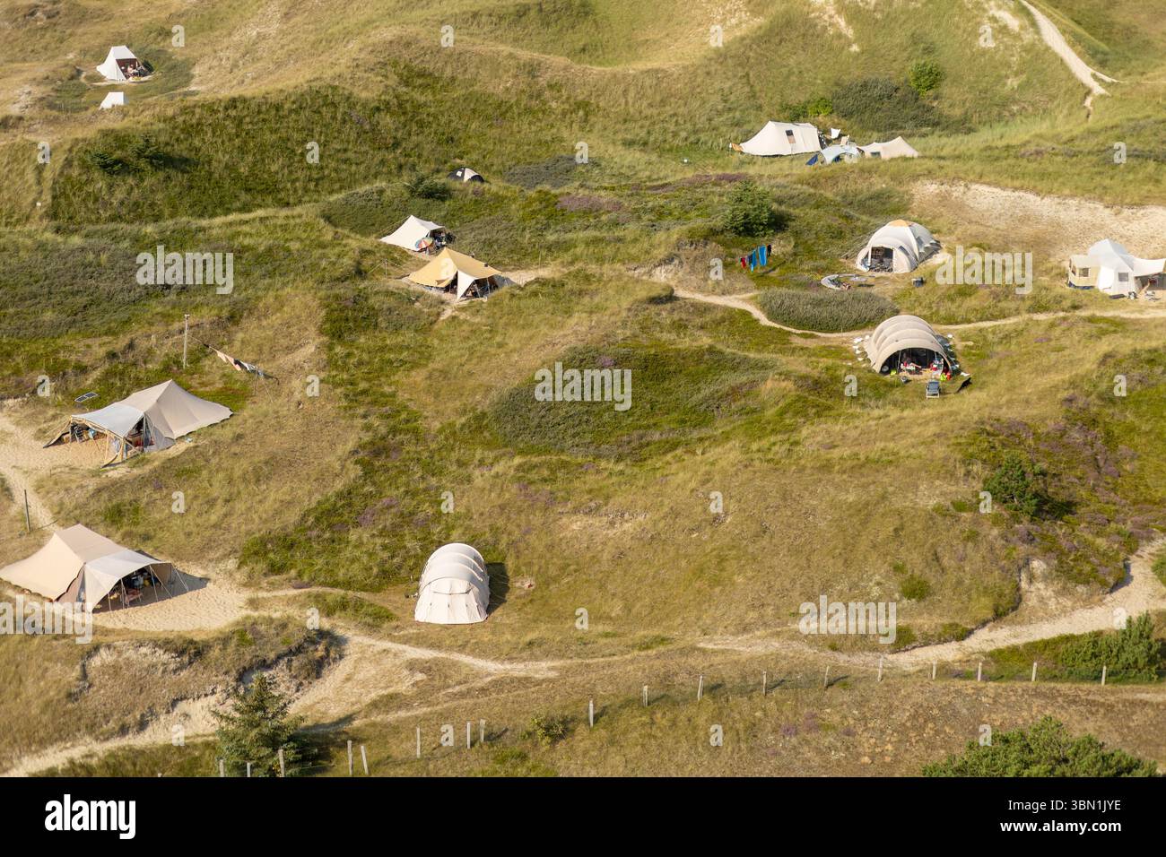 Le tende e i camper sono sparsi tra lussureggianti colline verdi, evidenziando una tranquilla esperienza di campeggio all'aperto circondati dalla natura. Il sole splende Foto Stock