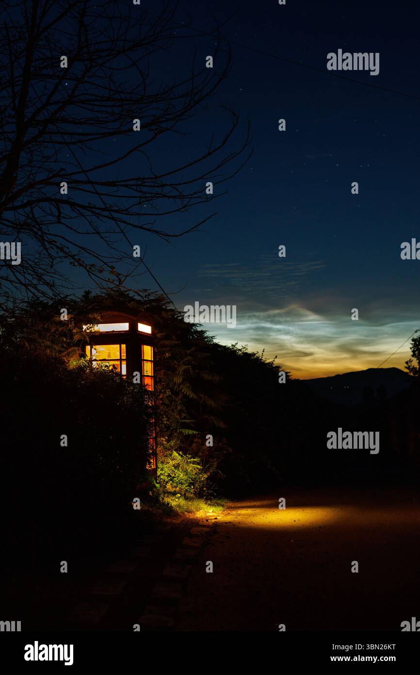 Cabina telefonica di notte sotto una notte nuvolosa di Noctilucent Foto Stock