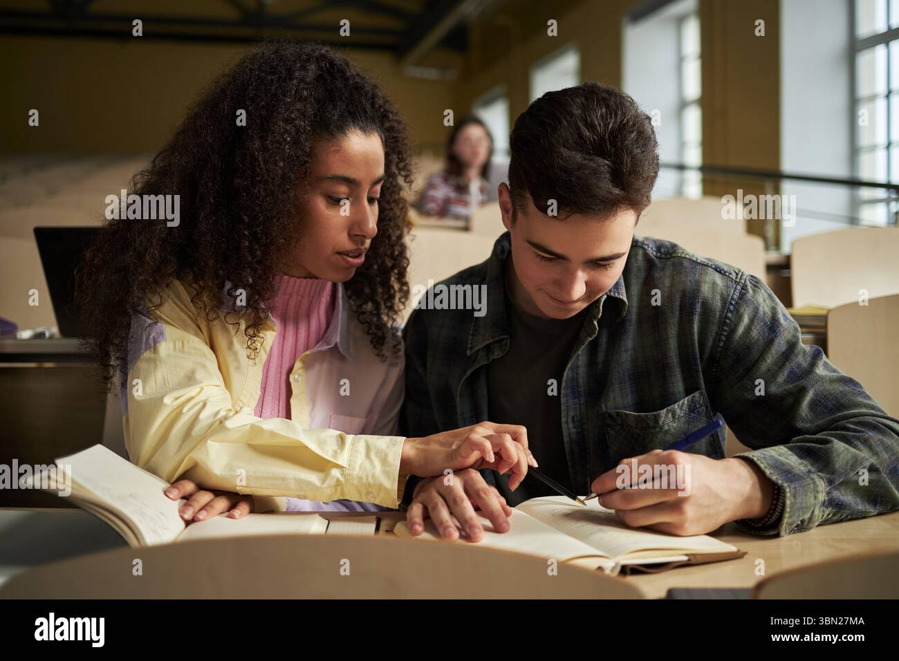 Giovane uomo caucasico e donna nera che studiano insieme in una sala conferenze universitaria, leggono libri di testo e prendono appunti, collaborano a compiti accademici, si concentrano sull'apprendimento Foto Stock