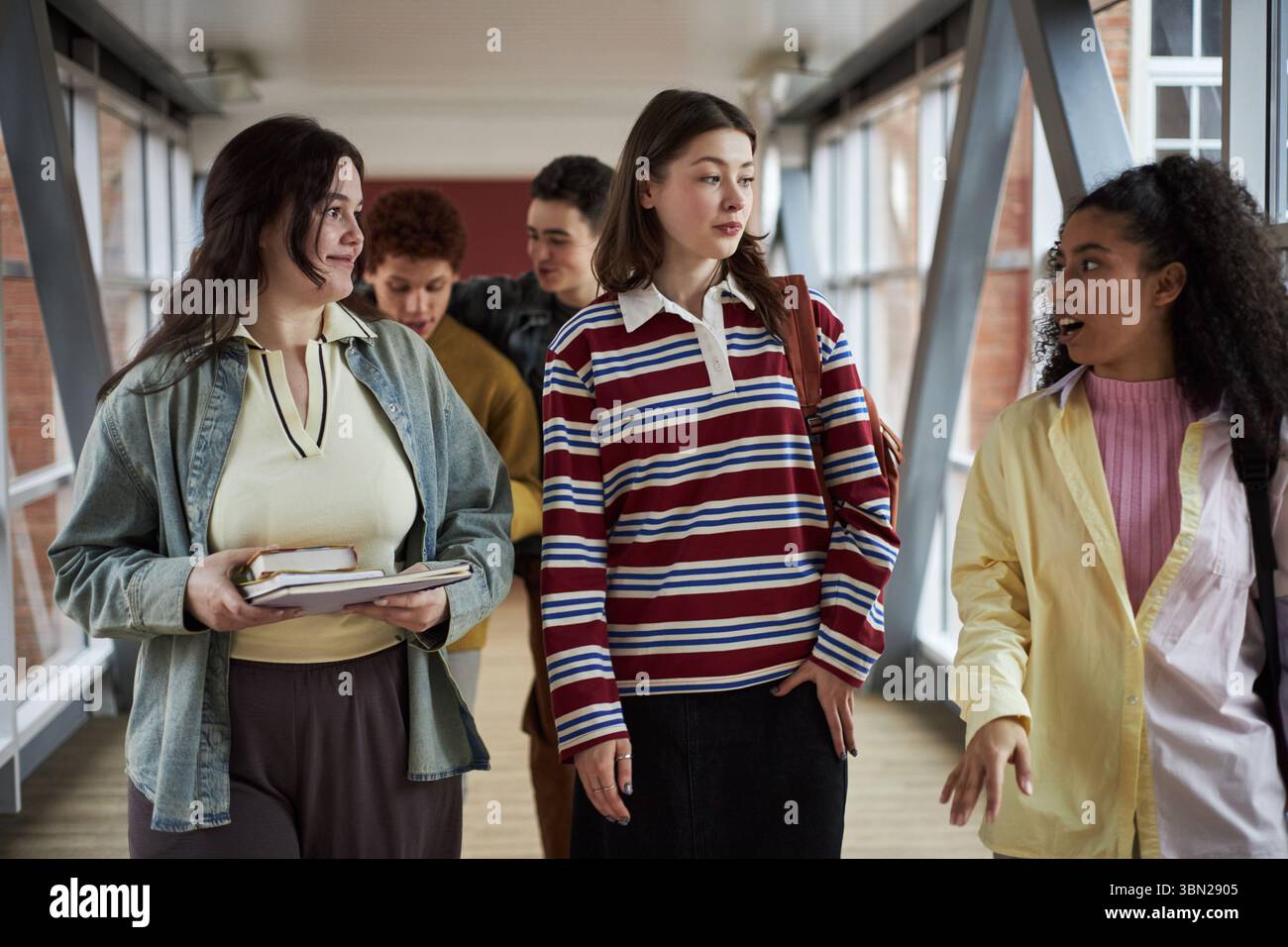 Gruppo di studenti universitari multietnici che camminano insieme nel corridoio, giovani donne e uomini che portano libri e zaini, si impegnano in conversazione mentre si recano in classe Foto Stock