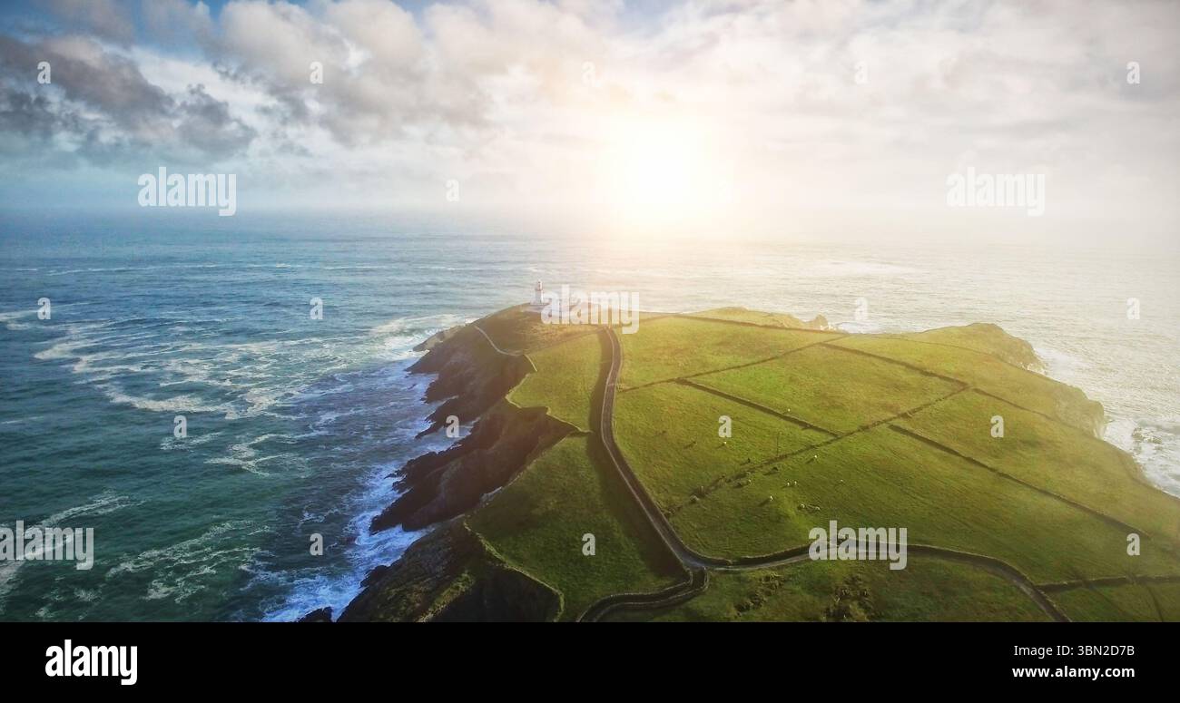 La penisola costiera erbosa, dal design piatto, mostra una strada tra i muri di pietra che conduce al faro Foto Stock