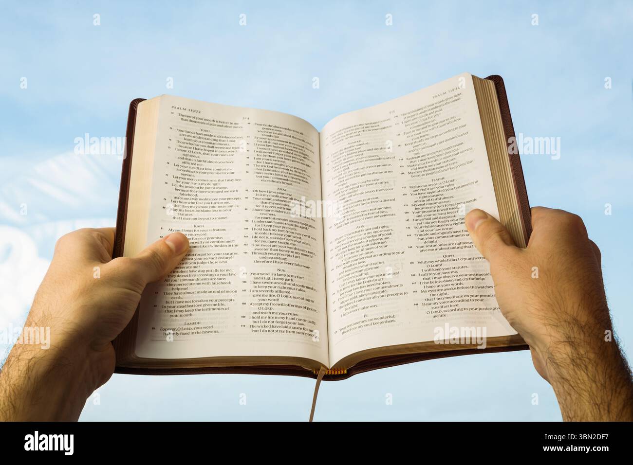 Primo piano di mani che tengono aperta la Bibbia contro il cielo Foto Stock
