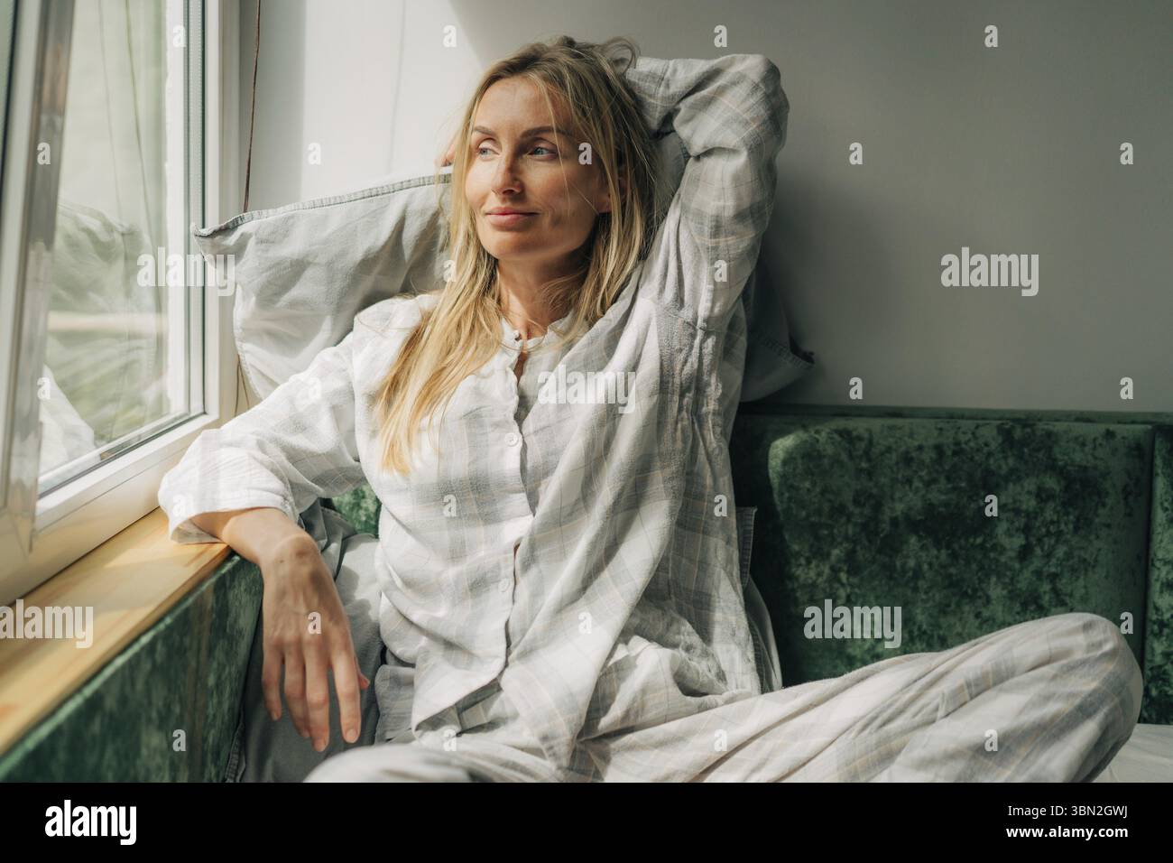 Bella donna in pigiama che guarda da una finestra Foto Stock