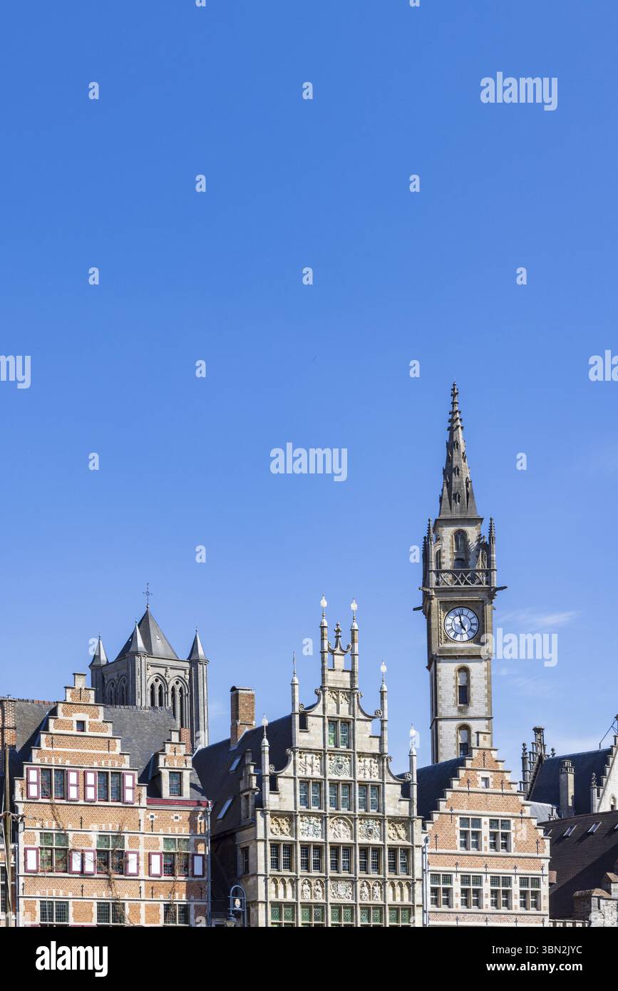 Antiche case a timpano e torre dell'orologio lungo il Korenlei nella città portuale di Gand nel nord-ovest del Belgio durante una giornata di sole Foto Stock