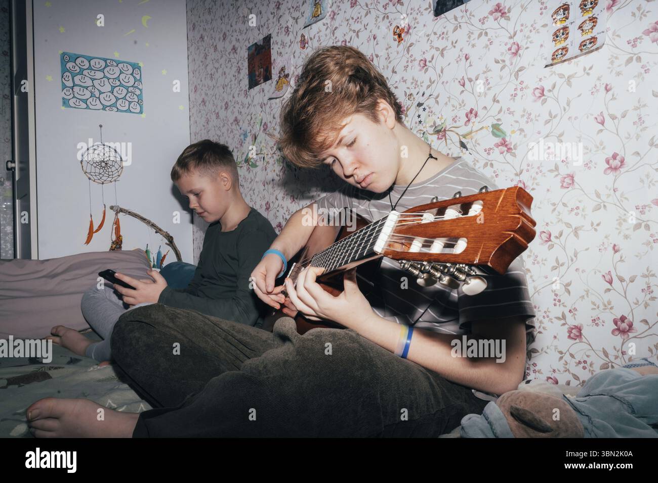 I bambini passano del tempo, la ragazza suona la chitarra, il ragazzo usa un telefono cellulare Foto Stock