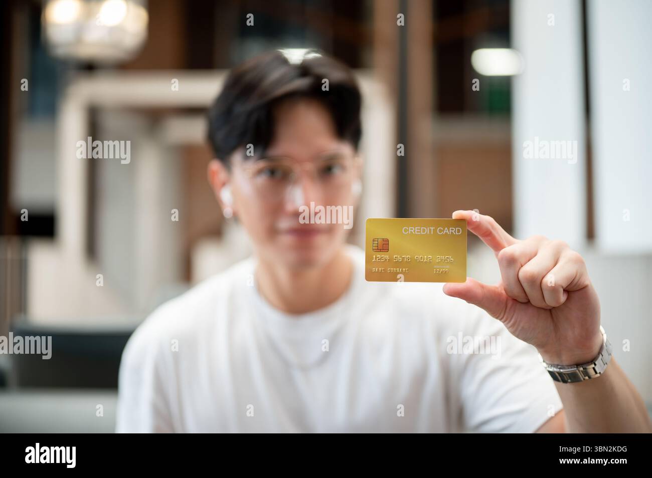 Uomo asiatico che indossa occhiali in maglietta bianca che tiene o mostra una carta di credito gialla. Pagamento con carta, pubblicità bancaria. Foto Stock