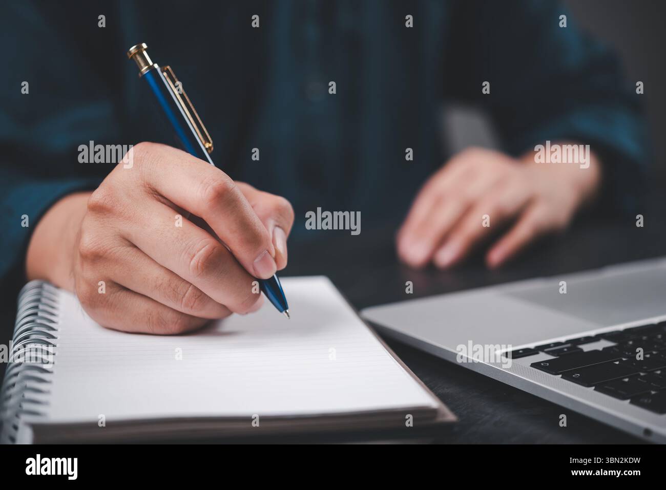 Scrittura a mano in primo piano su un notebook con una penna accanto al computer portatile. Formazione, pianificazione aziendale, configurazione di journaling con produttività e creatività dell'ambiente di lavoro moderni Foto Stock