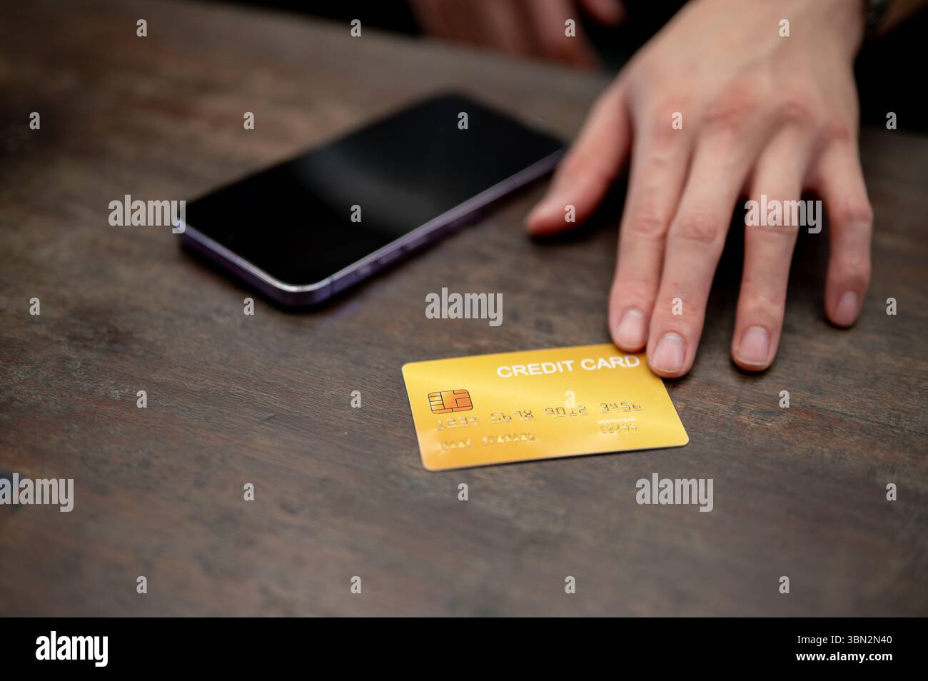 Primo piano di una mano che posiziona una carta di credito gialla accanto a uno smartphone su un tavolo di legno. Pagamento con carta, pubblicità bancaria. Foto Stock