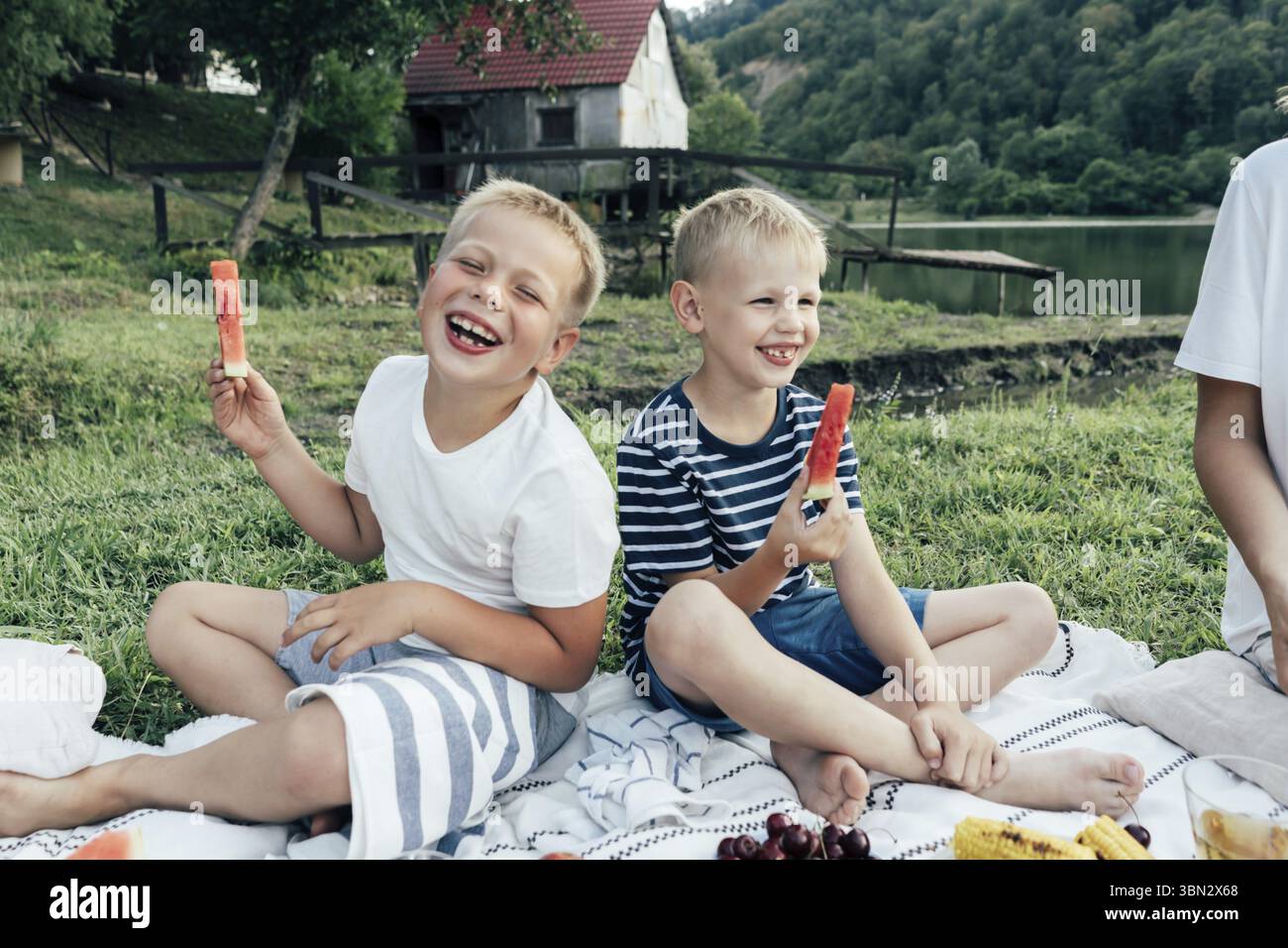 Due ragazzi preadolescenti ridono di gioia al picnic. I bambini tengono pezzi di anguria, mangiano raccolto fresco. Cibo sano durante le vacanze estive Foto Stock