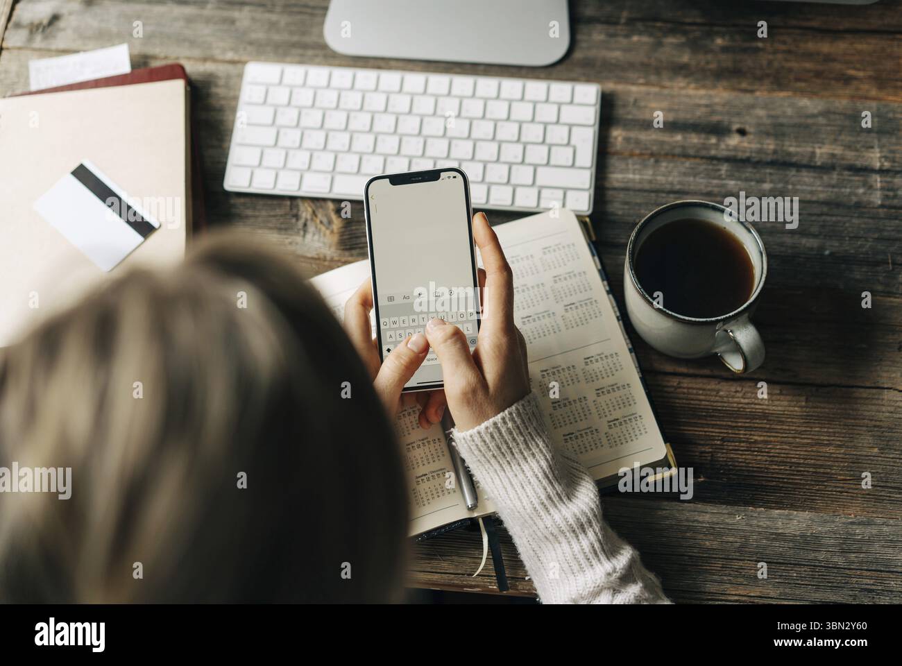 Draufsicht auf eine Frau, Die am Arbeitsplatz im Buero Notizen in das Telefon schreibt Foto Stock
