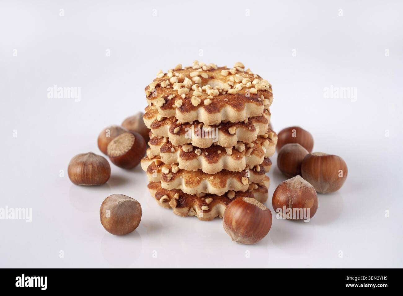 Una pila di biscotti di pasta frolla con noci e nocciole sparse su un bicchiere bianco Foto Stock