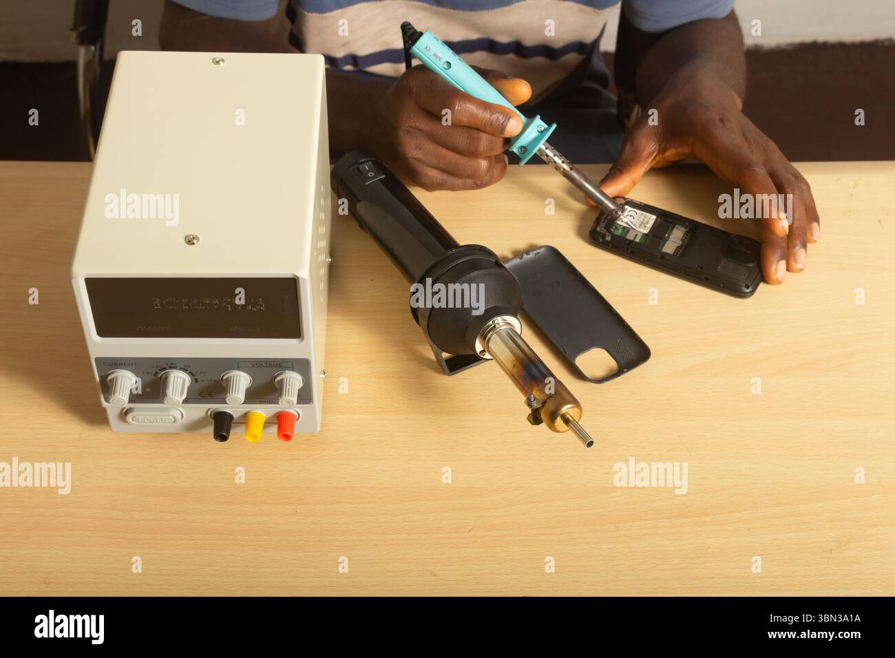 tecnico di primo piano per la riparazione di telefoni per saldatura con pistola termica unità di alimentazione digitale c.c. piano da tavolo per piccole imprese lavoro da parte di un imprenditore domestico Foto Stock