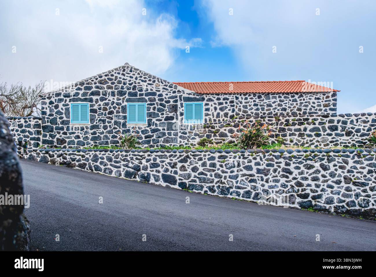Tradizionale casa in pietra delle Azzorre con pareti di roccia vulcanica nell'isola di Sao Jorge. Architettura portoghese atlantica, tegole in terracotta, persiane turchesi Foto Stock
