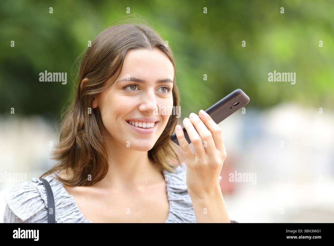 Donna felice che dice un messaggio al telefono che cammina per strada Foto Stock