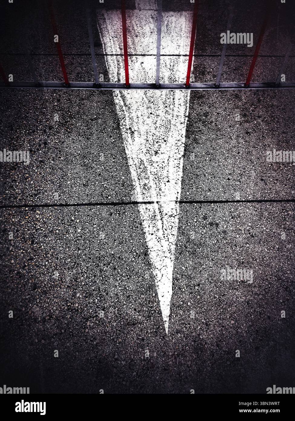 Una freccia bianca diagonale chiara punta sull'asfalto insieme a una barriera rossa. Foto Stock