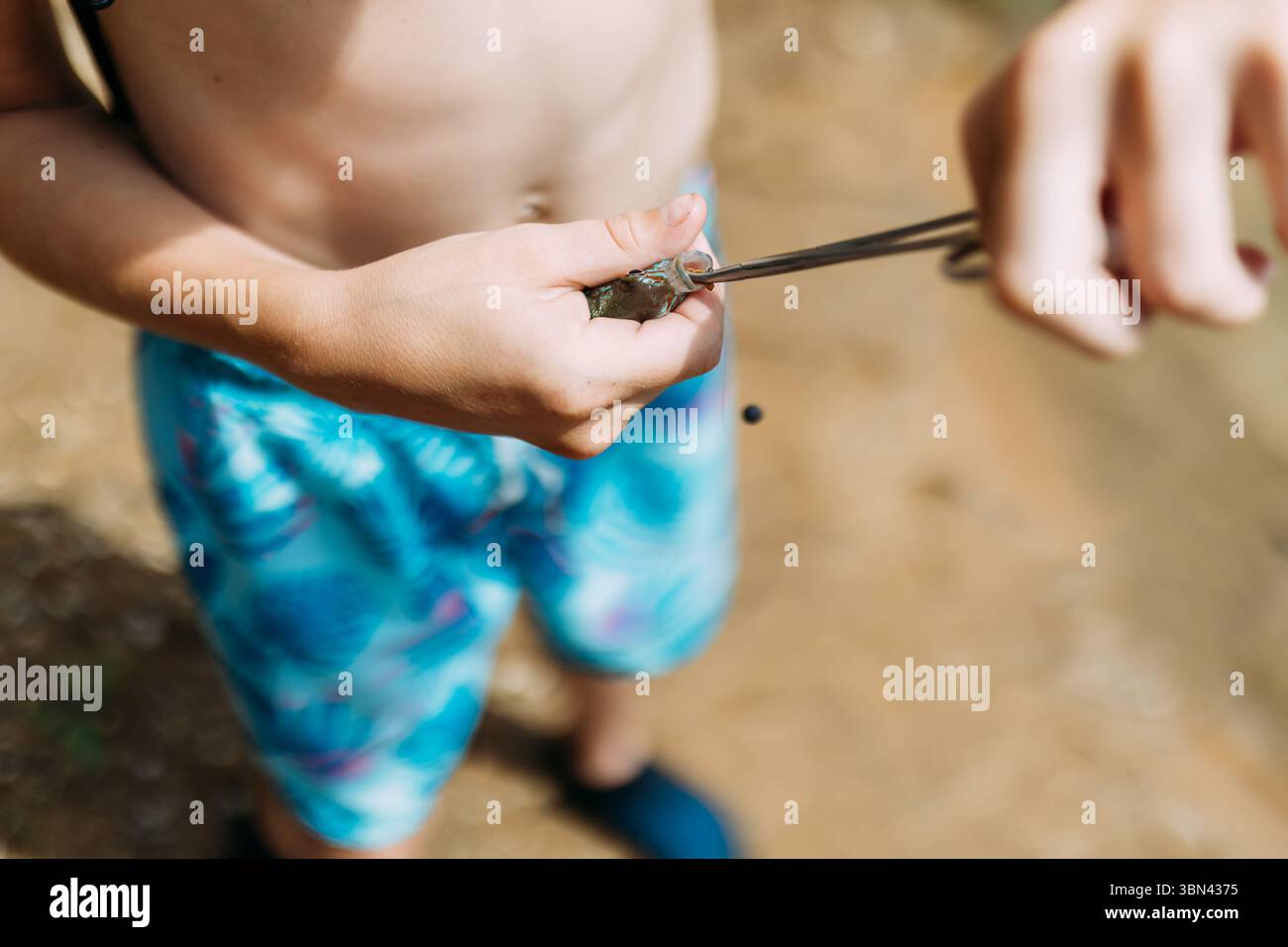 Ragazzo che sgancia il pesce con le pinze da pesca Foto Stock