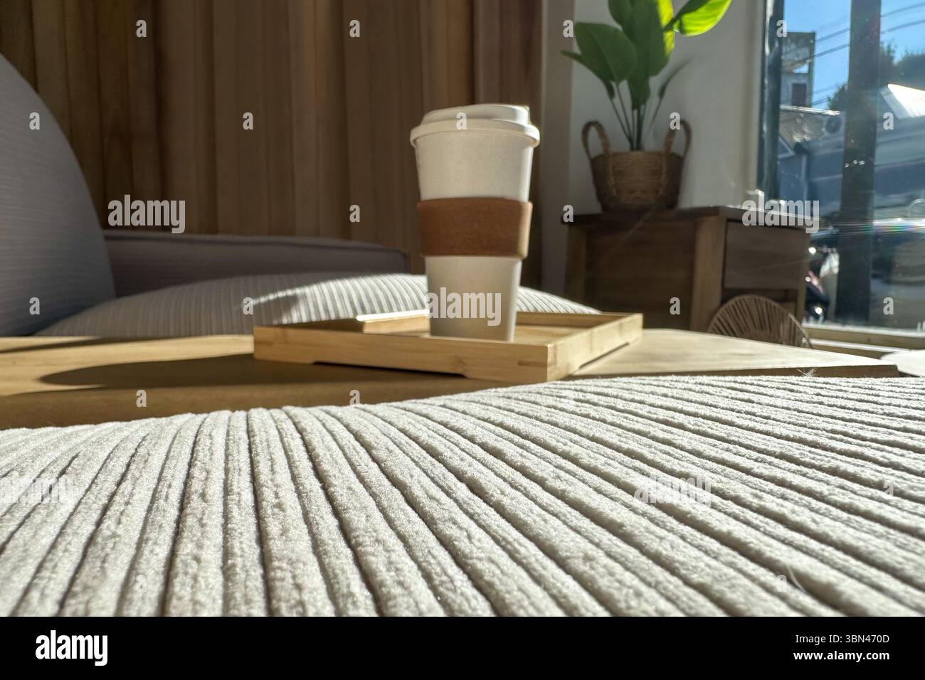 Accogliente divano letto con tessuti pastello, una tazza da caffè sul tavolo incassato, luce naturale che scorre attraverso la finestra e pareti di legno Foto Stock