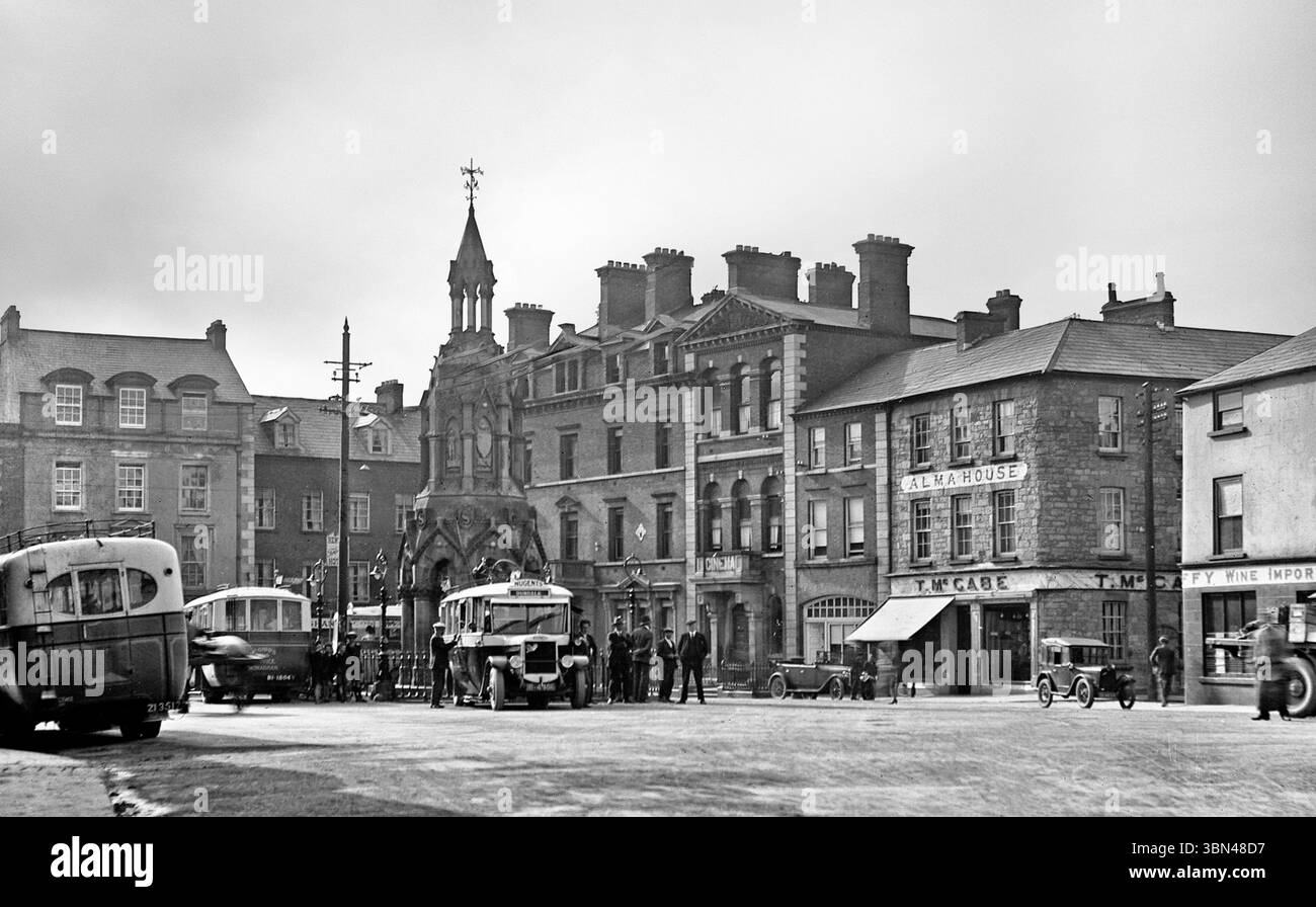 Una fotografia del Diamond dei primi anni del XX secolo, con auto e pullman d'epoca. La più centrale delle quattro piazze della città di Monaghan, il suo impressionante monumento è chiamato Rossmore Memorial, ed è stato eretto in onore del IV barone Rossmore. Morì nel 1874 in un incidente durante una corsa in steeplechase irlandese, all'età di ventidue anni. Foto Stock
