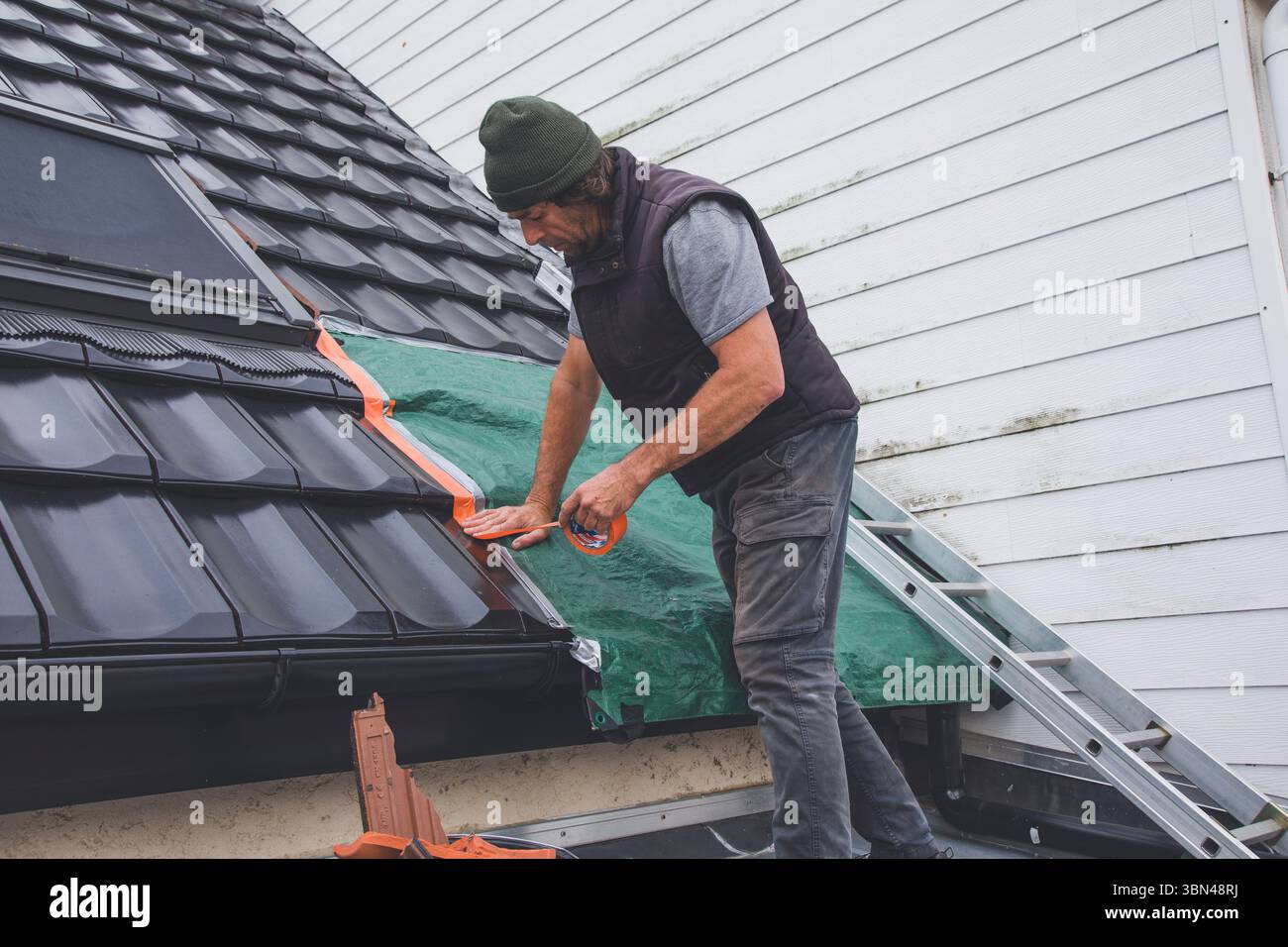 Conciatetto che installa una tela cerata in caso di maltempo in attesa di lavoro Foto Stock