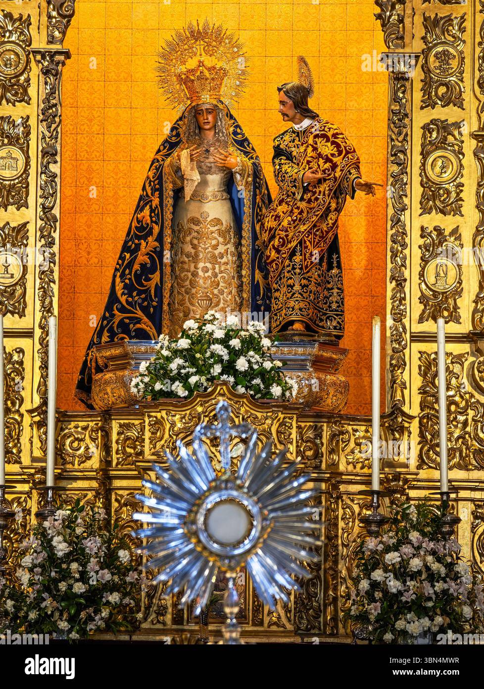 Il Santissimo Sacramento si illumina di calore davanti all'altare della Vergine di la Amargura, circondato da fiori e candele scintillanti. Foto Stock