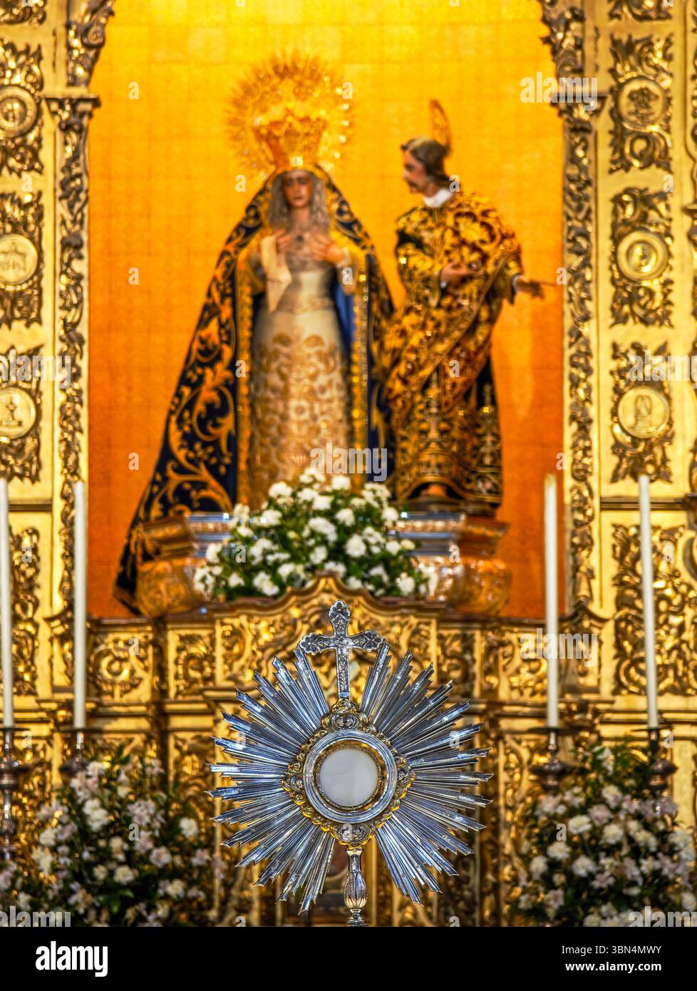 Il Santissimo Sacramento si illumina di calore davanti all'altare della Vergine di la Amargura, circondato da fiori e candele scintillanti. Foto Stock