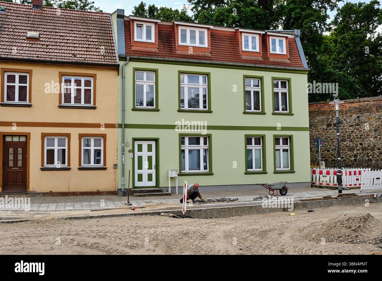 25 giugno 2023 - Neubrandenburg-Germania: Lavori stradali in progres con asfaltatrici in lastricato in Germania una strada residenziale fiancheggiata da uno storico colorato Foto Stock