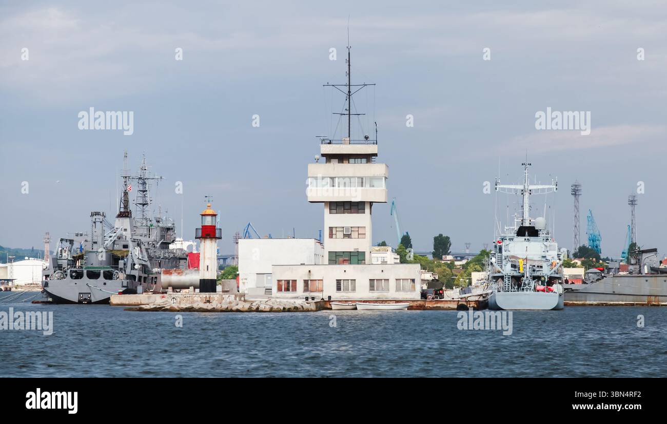 Porto navale con grandi navi militari attraccate accanto a una moderna torre di controllo e vista panoramica sul mare. Porto di Varna, Bulgaria Foto Stock