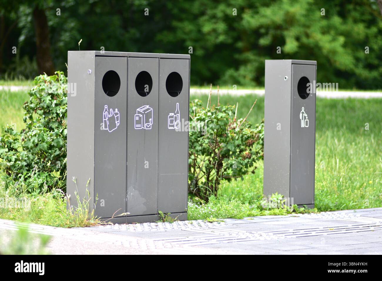 Smistamento dei contenitori dei rifiuti in un parco pubblico con contenitori separati per plastica, carta e vetro a sinistra e rifiuti generici a destra. Contrassegno di messa a terra Foto Stock