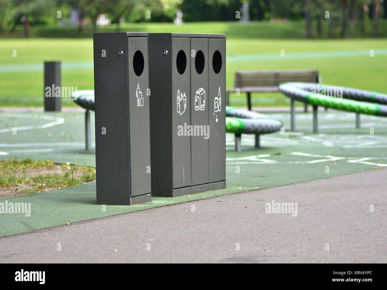 Lo smistamento dei contenitori dei rifiuti in un parco pubblico con contenitori separati per plastica, carta, vetro e rifiuti generici promuove la sostenibilità e la responsabilità Foto Stock