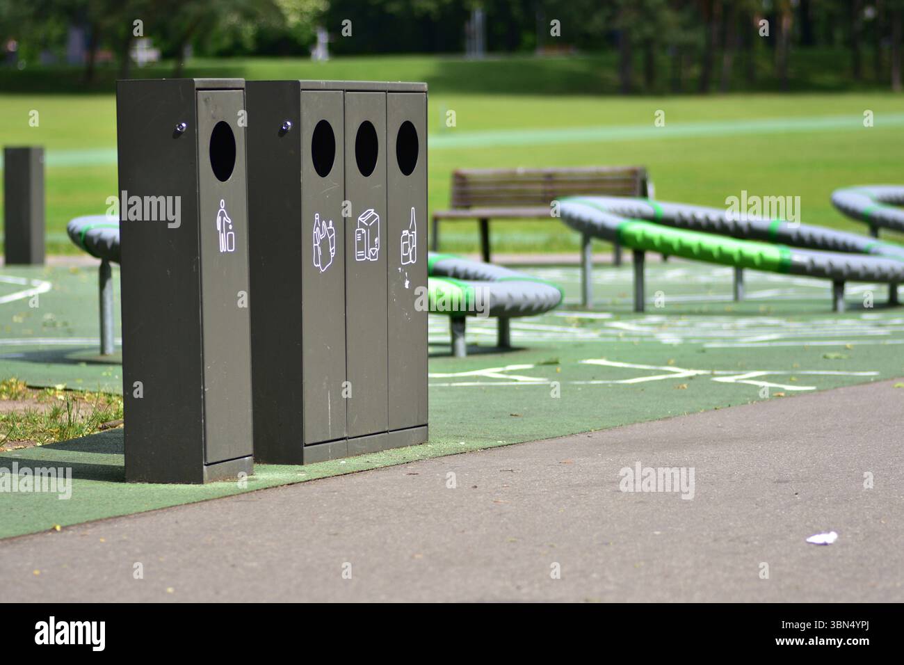 Lo smistamento dei contenitori dei rifiuti in un parco pubblico con contenitori separati per plastica, carta, vetro e rifiuti generici promuove la sostenibilità e la responsabilità Foto Stock