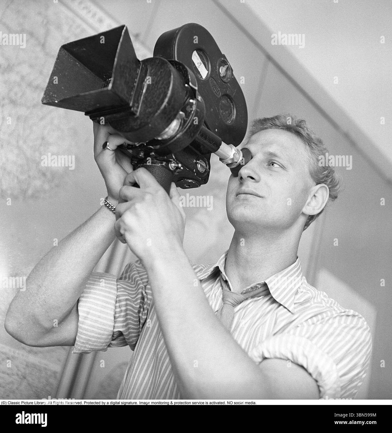 The Man with the Film camera 1950. Un uomo tiene in mano una macchina fotografica e guarda attraverso il suo mirino. Il modello è un Arriflex 35 i o II, prodotto dalla società tedesca ARRI (Arnold & Richter). Questo modello di fotocamera rivoluzionò l'industria cinematografica con il suo design innovativo e la sua facilità d'uso ed è stato ampiamente utilizzato negli anni '1950, in particolare in newsreel, documentari e produzione di lungometraggi, grazie alla sua portabilità e affidabilità. Svezia 1950. Foto Stock