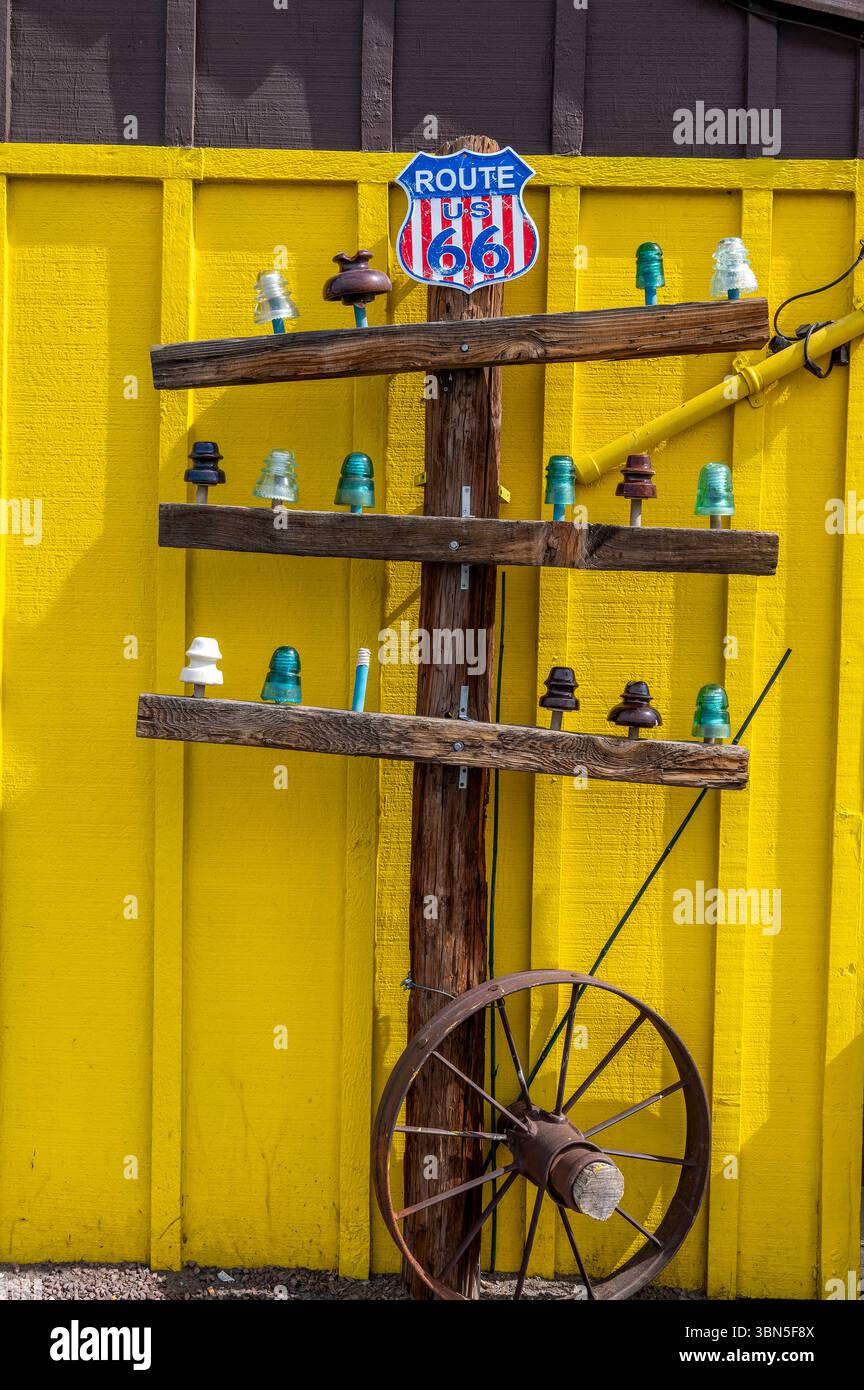 Mostra vintage Route 66 con isolanti in vetro colorato e ruota per carri su una parete in legno giallo brillante a Seligman, Arizona, che simboleggia l'americana Foto Stock