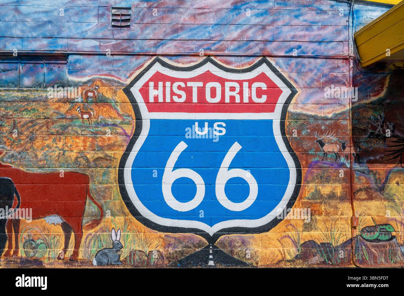 Colorato murale dello scudo della storica Route 66 dipinto su un muro a Seligman, Arizona, circondato dalla fauna selvatica del deserto e dal paesaggio sudoccidentale. Foto Stock