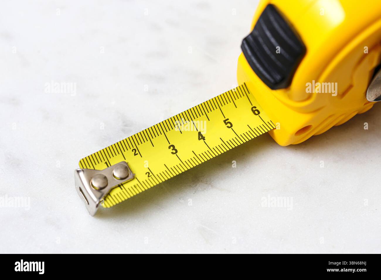 Metro a nastro giallo su sfondo bianco. Utensile per lavori di ristrutturazione e costruzione di abitazioni. Precisione in centimetri. Isolato su marmo bianco. Foto Stock