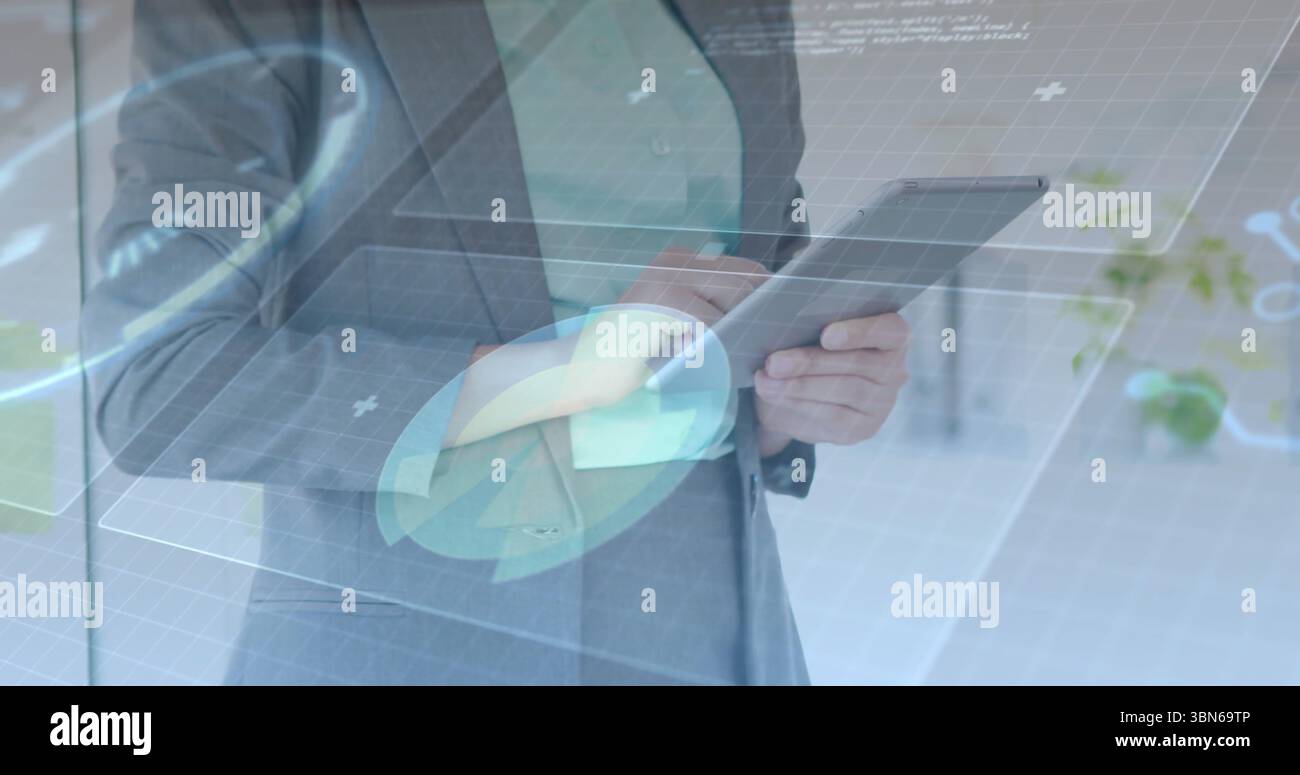 Con un tablet, un dirigente in tuta grigia che utilizza l'interfaccia utente olografica in ufficio con grafici a griglia e icone Foto Stock