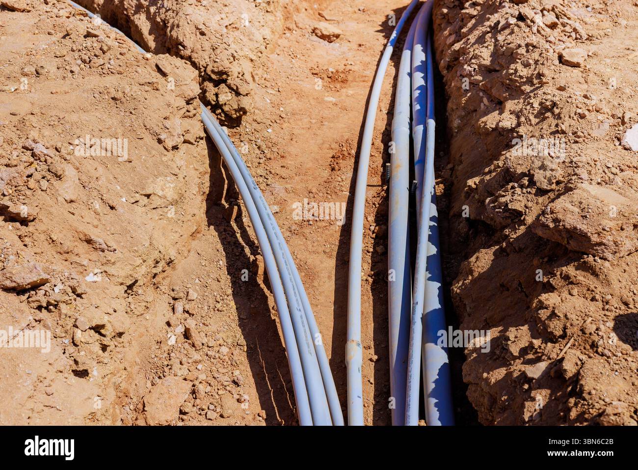 I lavoratori installano vari tubi elettrici in fossati profondi nei cantieri edili Foto Stock