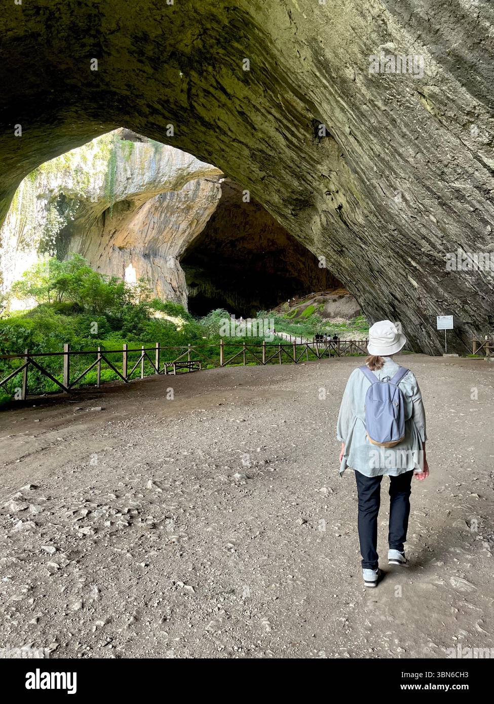 Il turista sta sta sta entrando nella massiccia apertura della Grotta di Devetashka, una meraviglia naturale mozzafiato nei Balcani della Bulgaria, nell'Europa orientale e nei Balcani - Immagine stock catturata con smartphone