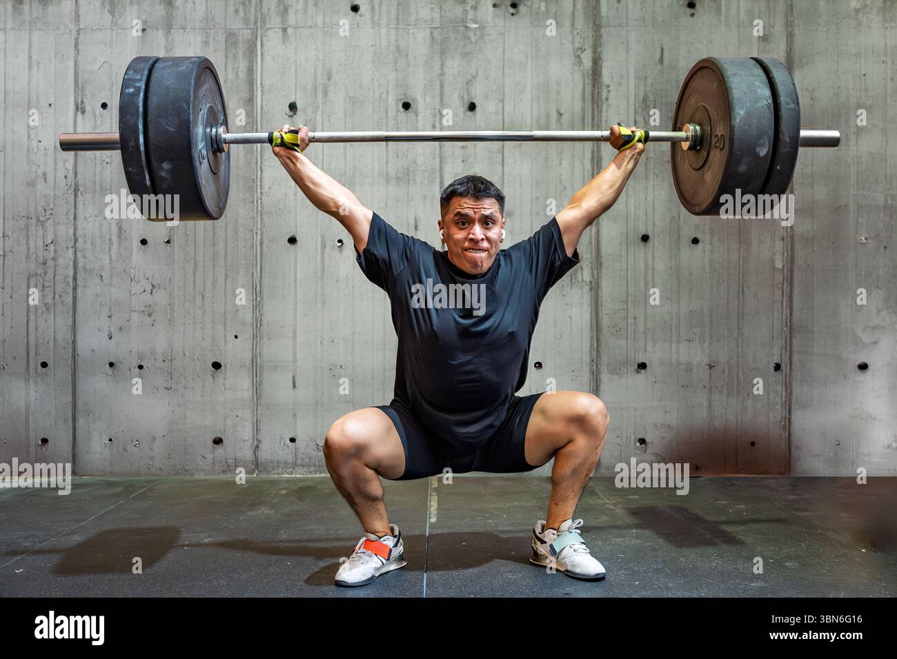 Un atleta di sollevamento pesi esegue uno squat sospeso in una palestra, mostrando forza e tecnica in condizioni difficili. Foto Stock