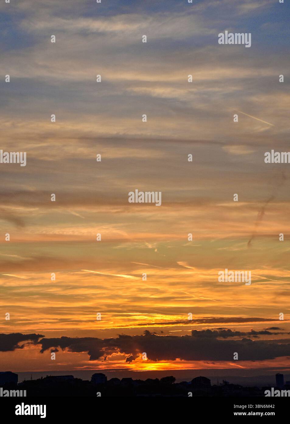 Spettacolari tramonti con cielo acceso e sagome da edificio, calde tonalità arancioni dominano lo skyline della città al tramonto. Foto Stock