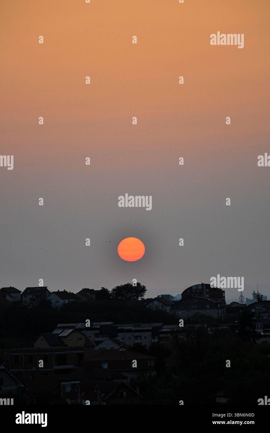 Skyline della città sotto il tramonto dorato, cielo vibrante sfumato che mescola tonalità arancione, blu e grigio in un'atmosfera tranquilla al crepuscolo Foto Stock