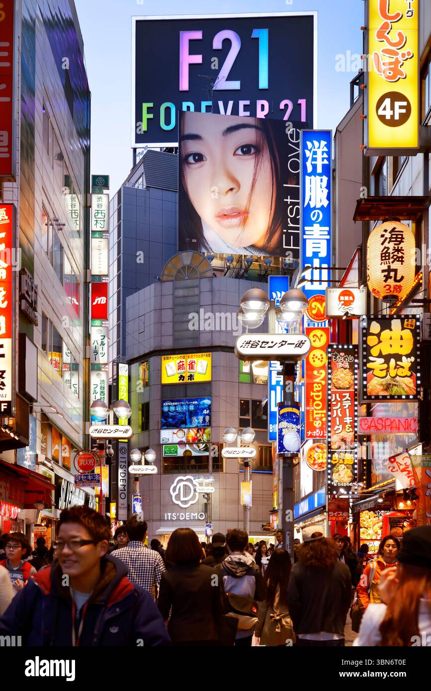 Gente sulle strade di Shibuya illuminata con cartelli colorati la sera. Utada Hikaru, primo amore e per sempre 21 cartelloni. Tokyo, Giappone Foto Stock
